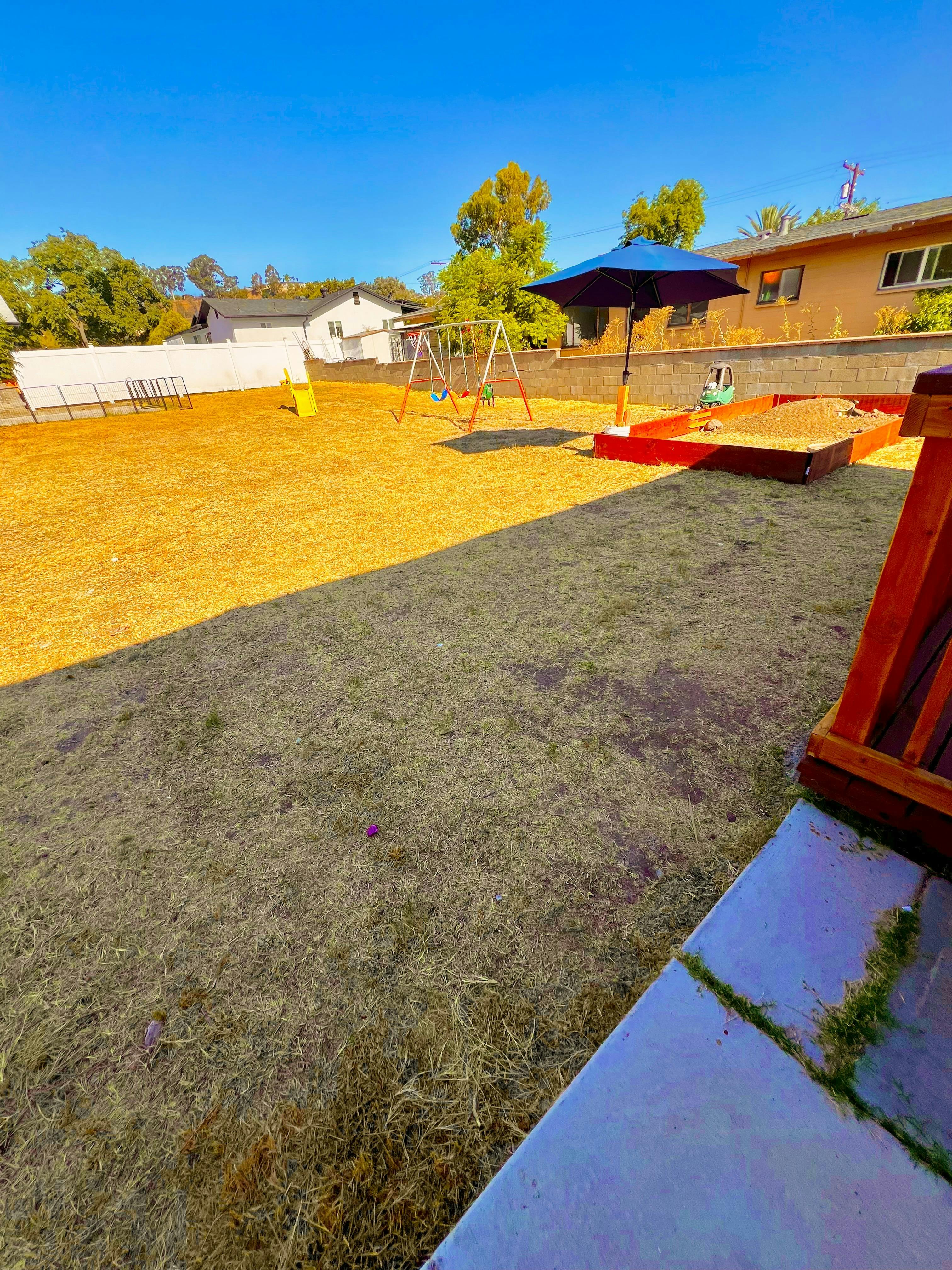 Backyard with a swing set, sandbox, and blue umbrella