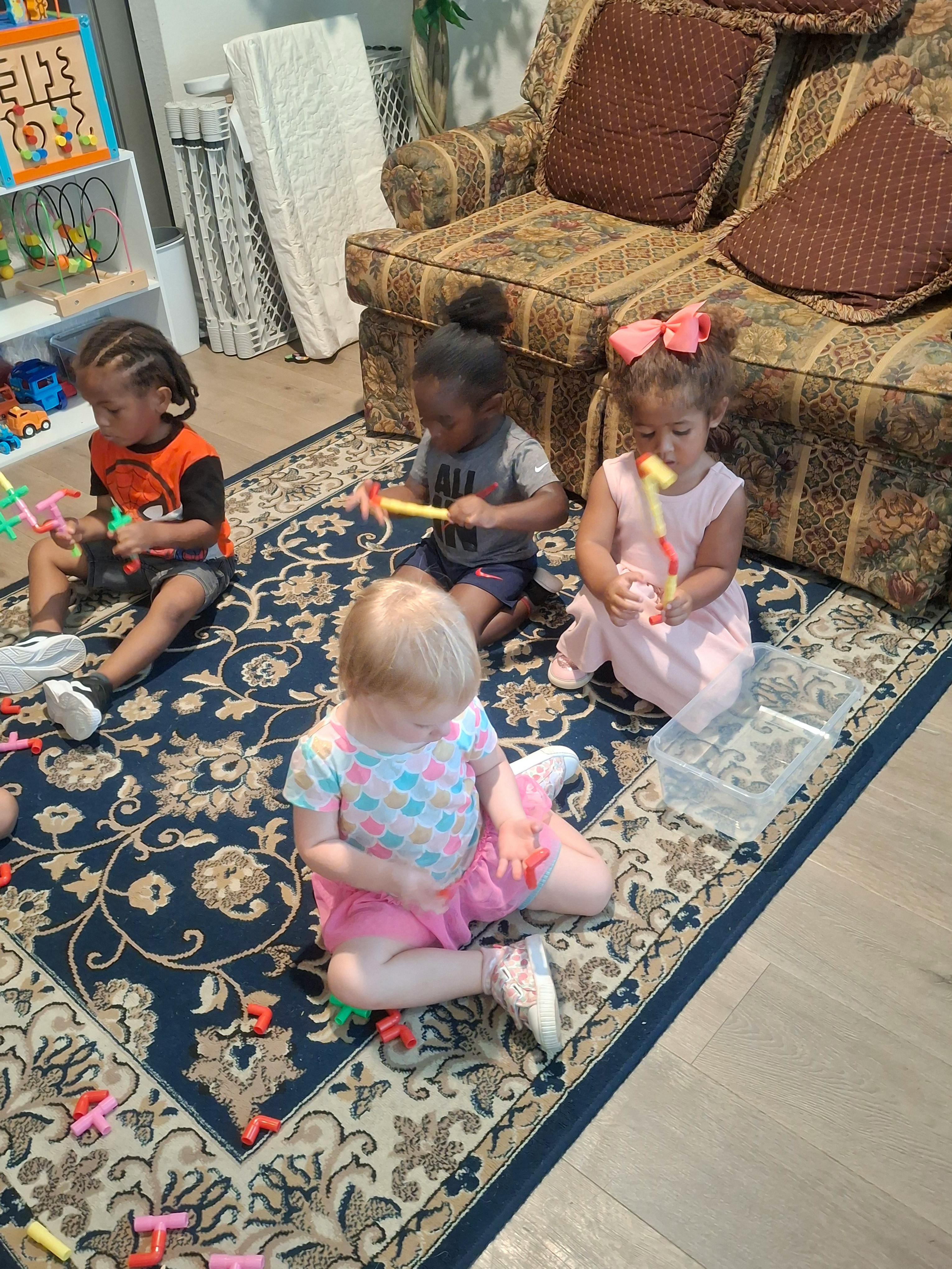 Four children sitting on a patterned rug playing with building toys