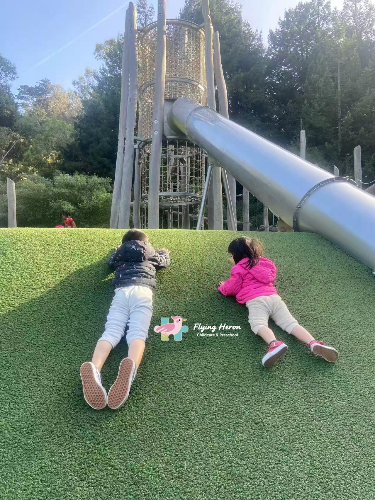 Two children climbing a grassy hill on a playground