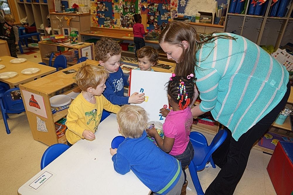 Adult and multiple children gathered around a table in a classroom