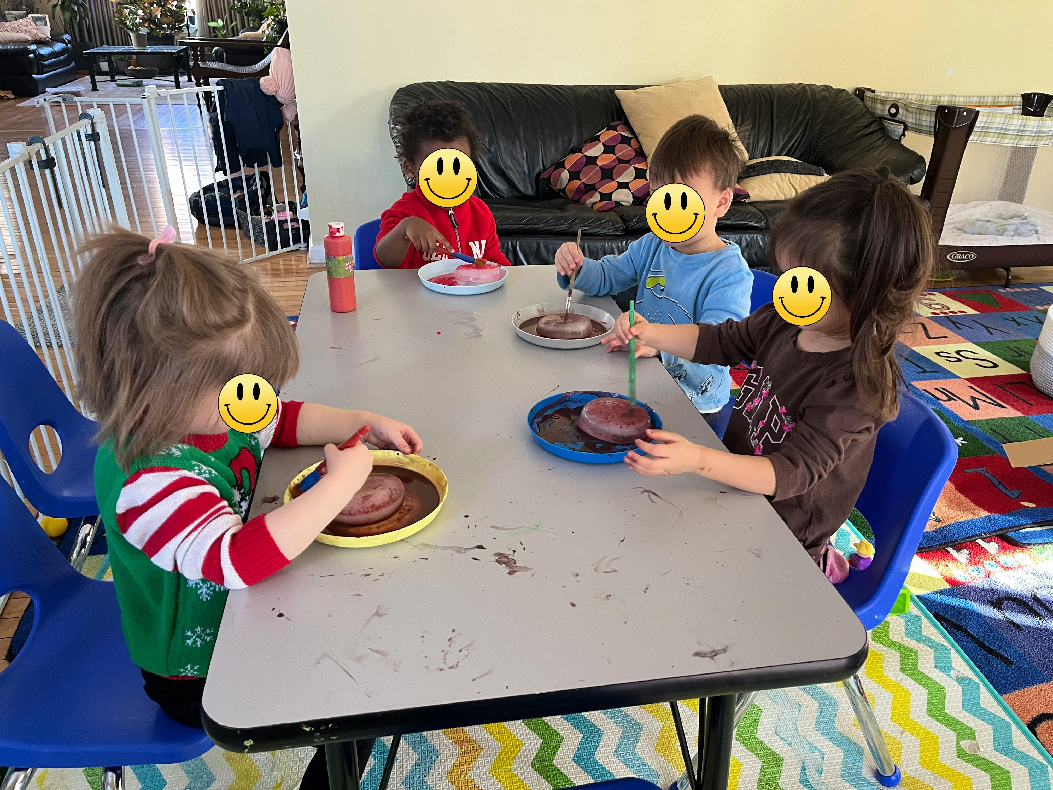 Four children painting objects on plates at a table