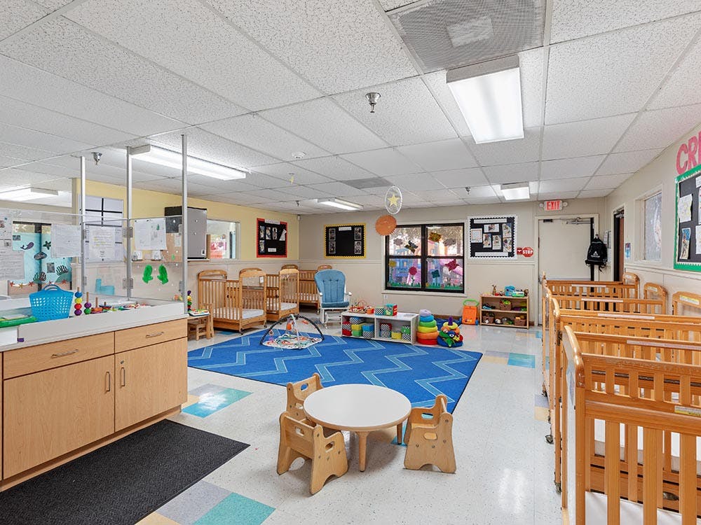 A childcare classroom with cribs, play mats, and small tables