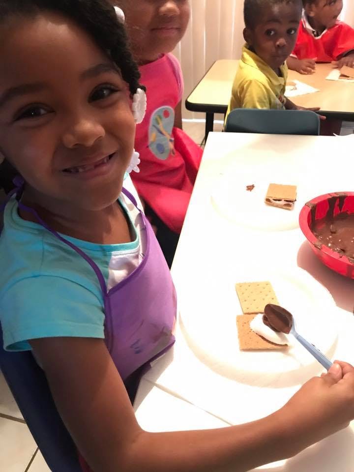 Child making s'mores with chocolate and marshmallows on a graham cracker