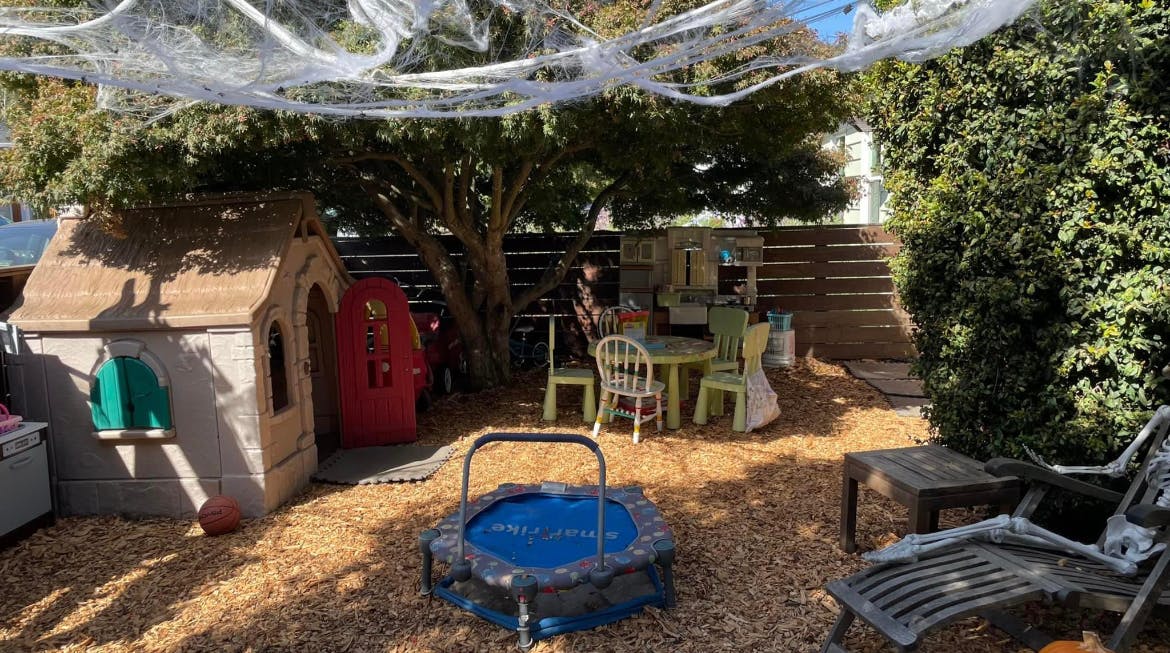 Backyard with playhouse, trampoline, and outdoor furniture under spiderwebs