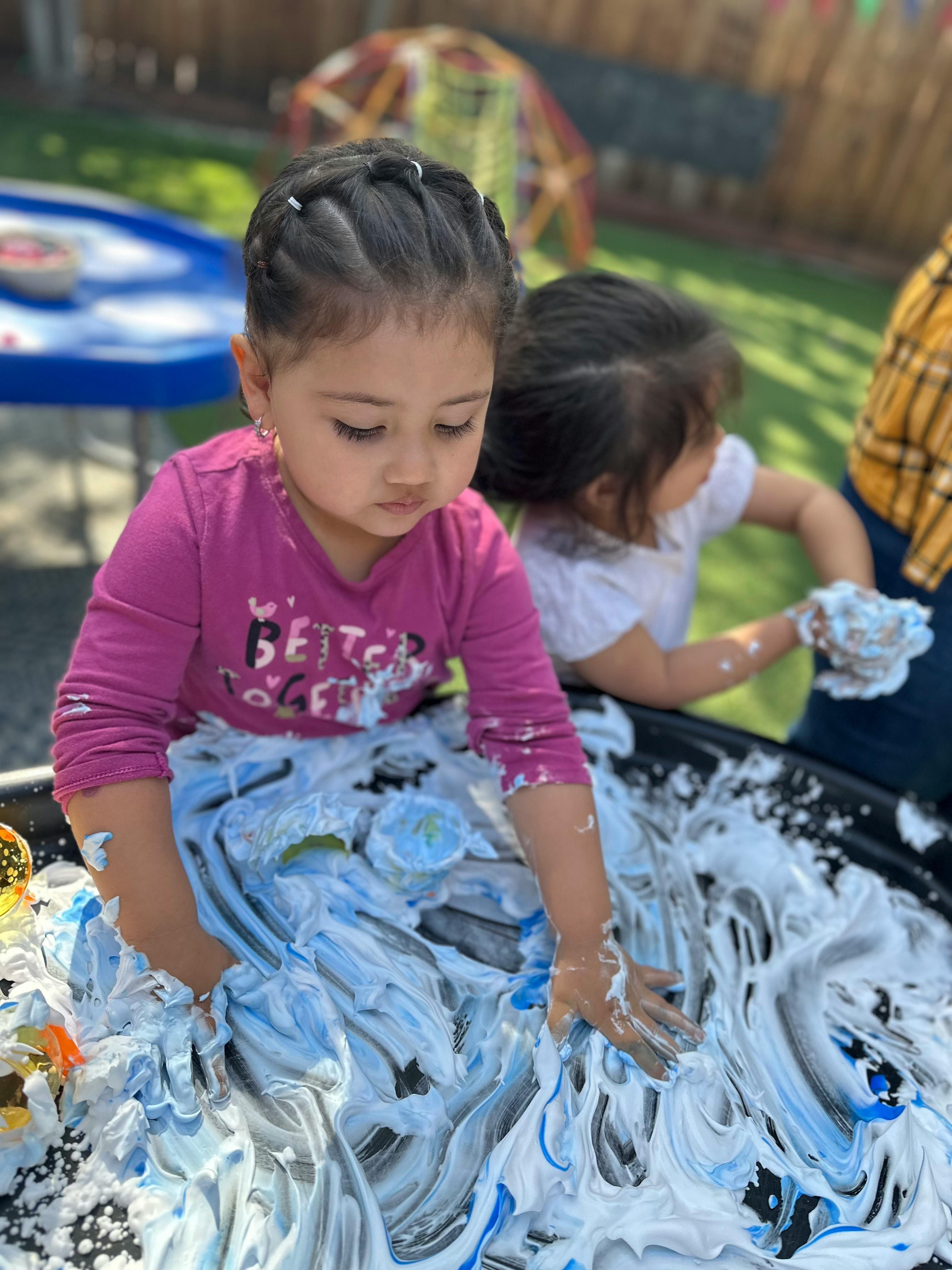 Child playing with shaving cream and blue paint in a tray