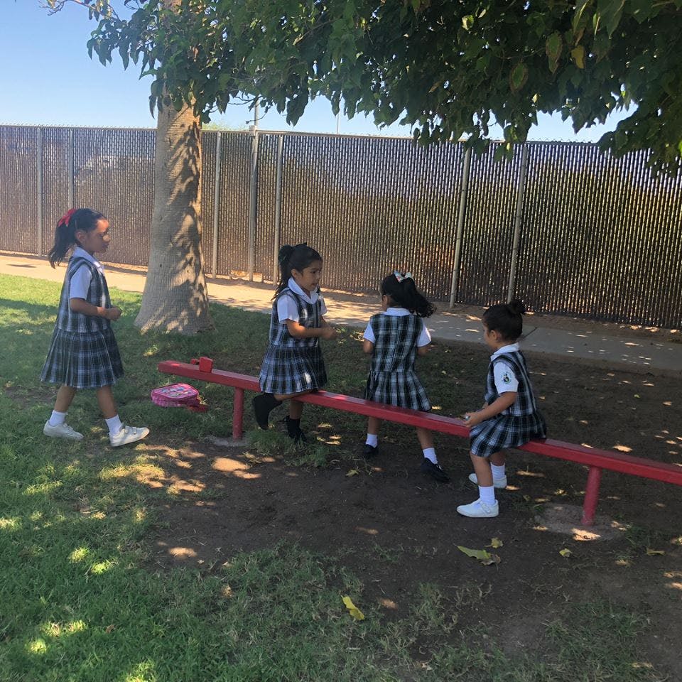 Three children in plaid uniforms playing on a seesaw
