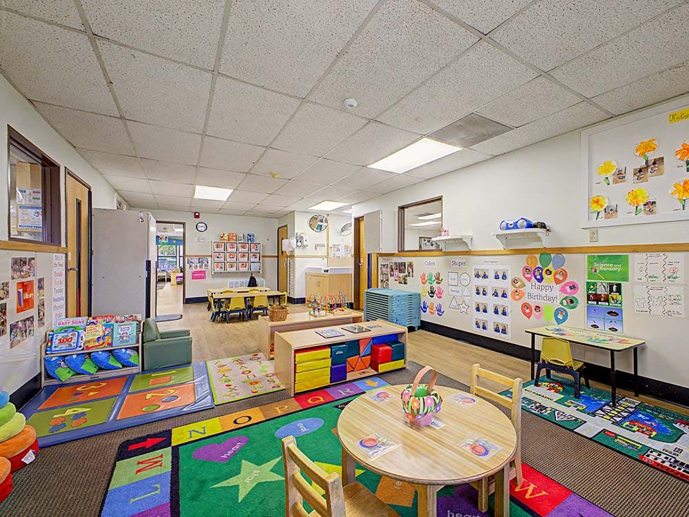 Colorful classroom with rugs, small tables and chairs, and learning decorations on walls