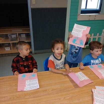 Children sitting at a table with pink craft papers featuring handprints