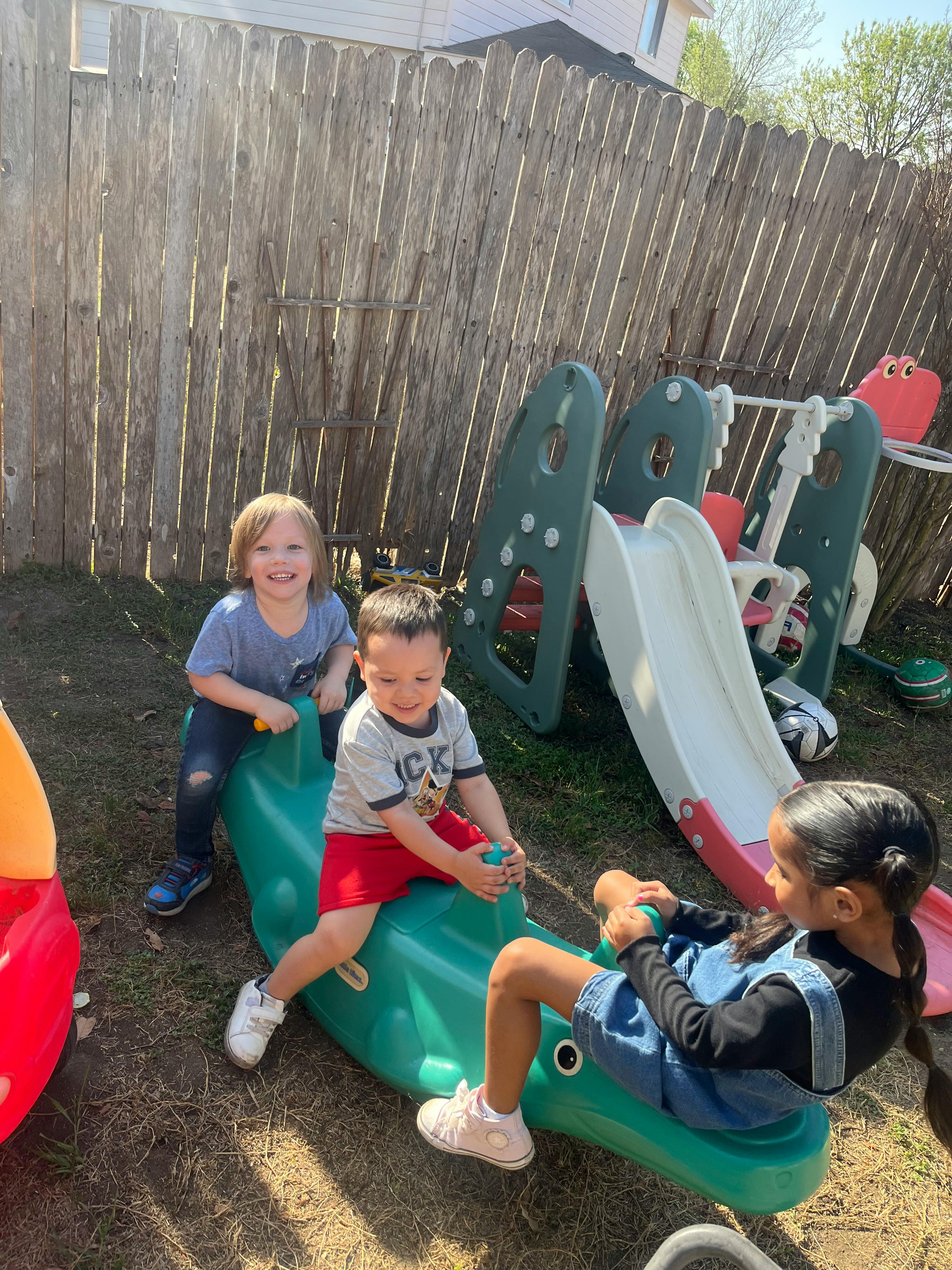 Three children playing on a seesaw and slide in a backyard