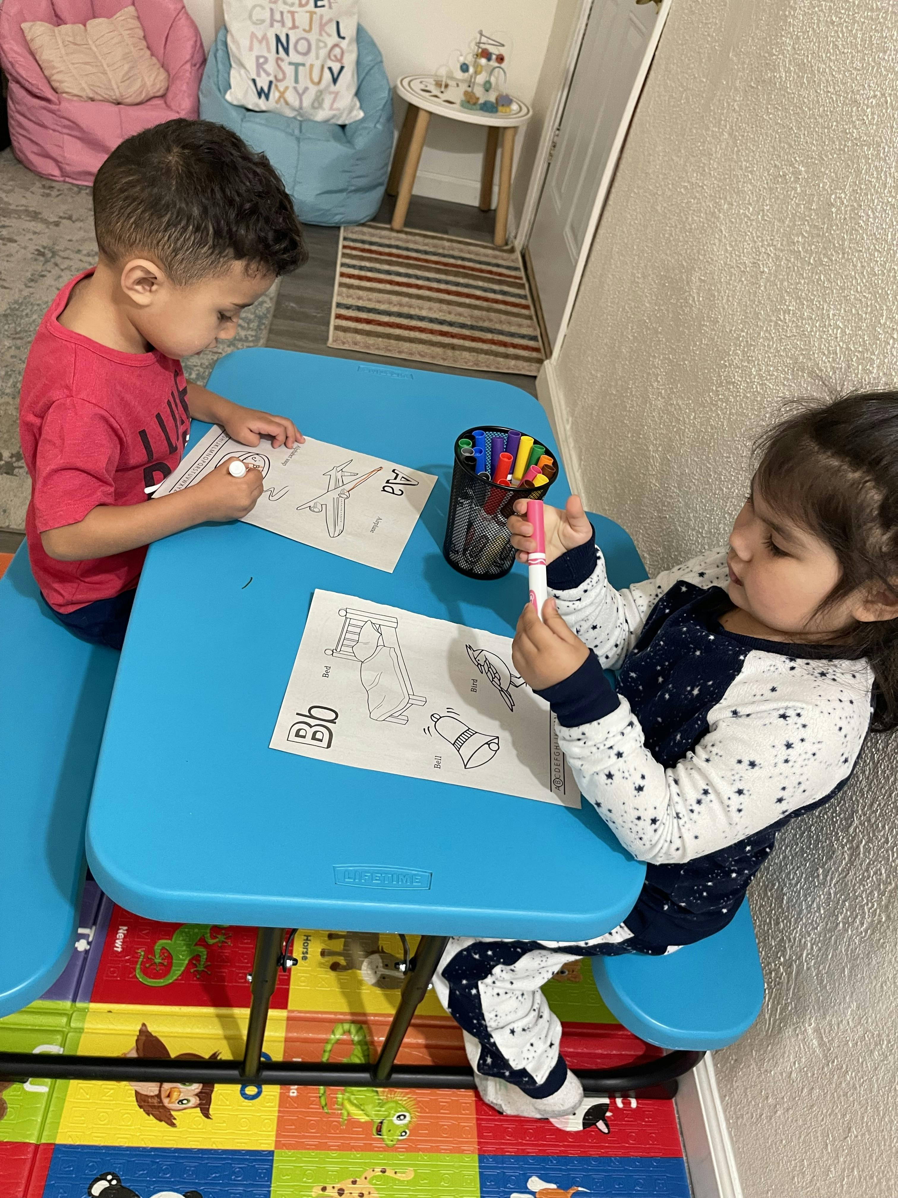 Two children coloring activity sheets at a blue table