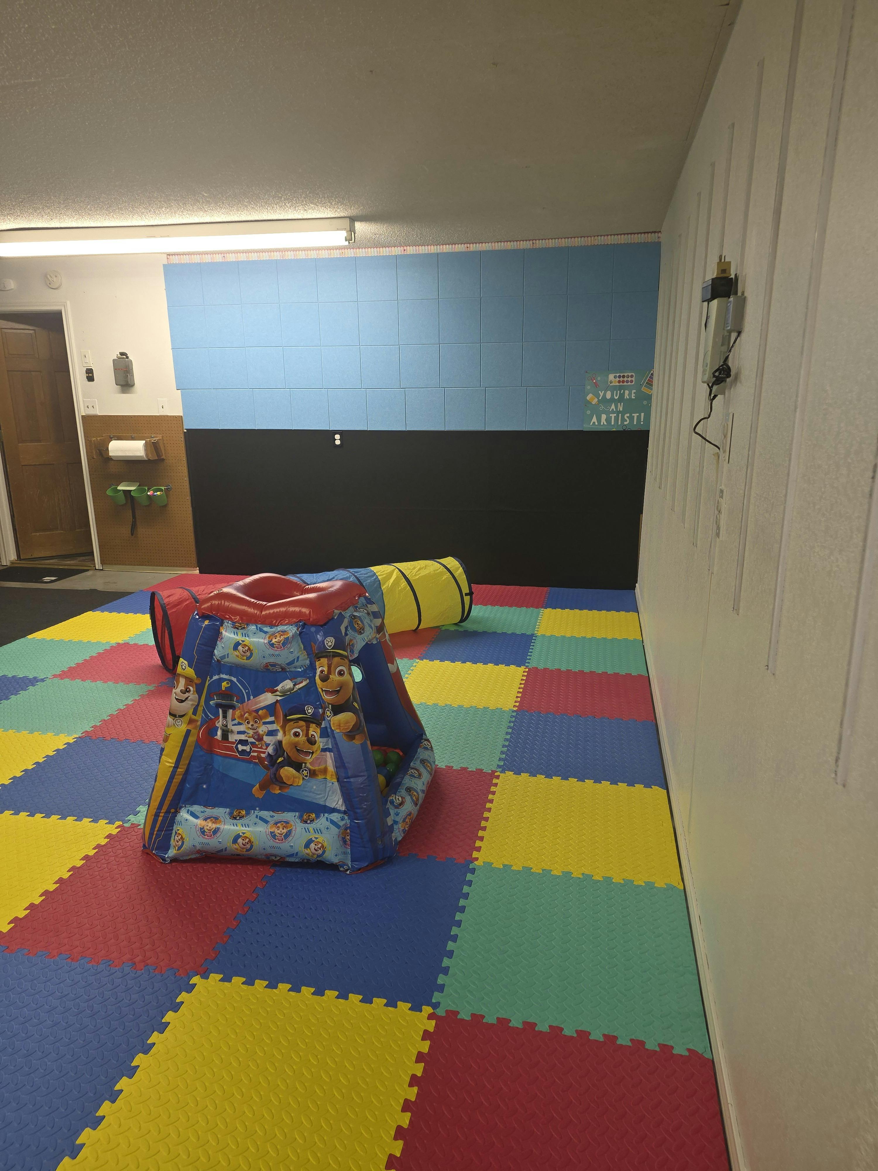 Play area with colorful floor mats, a play tent, and a tunnel