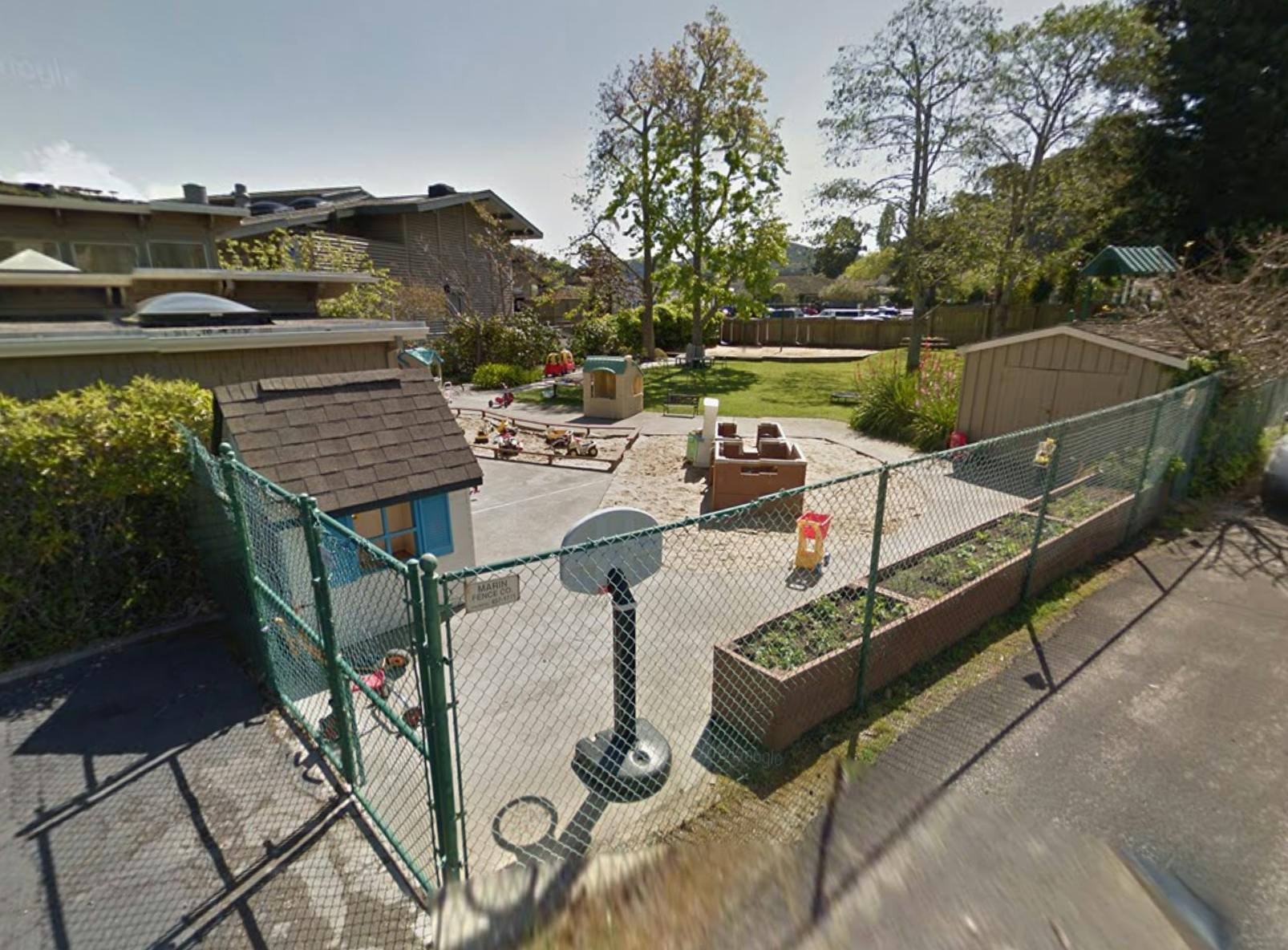 Outdoor playground with a small playhouse, basketball hoop, and fenced area