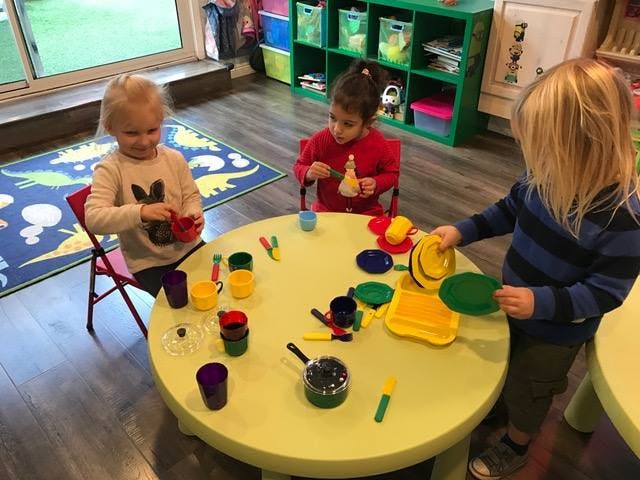 Three children playing with toy dishes at a table in a classroom
