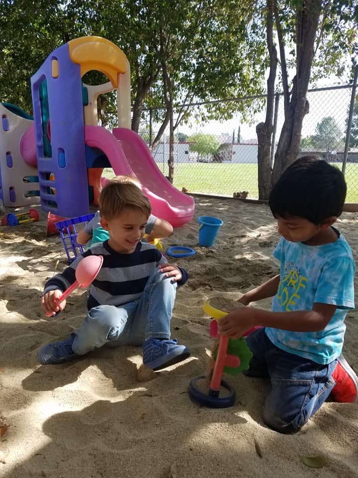 Two children playing in a sandbox with toys near a playground slide