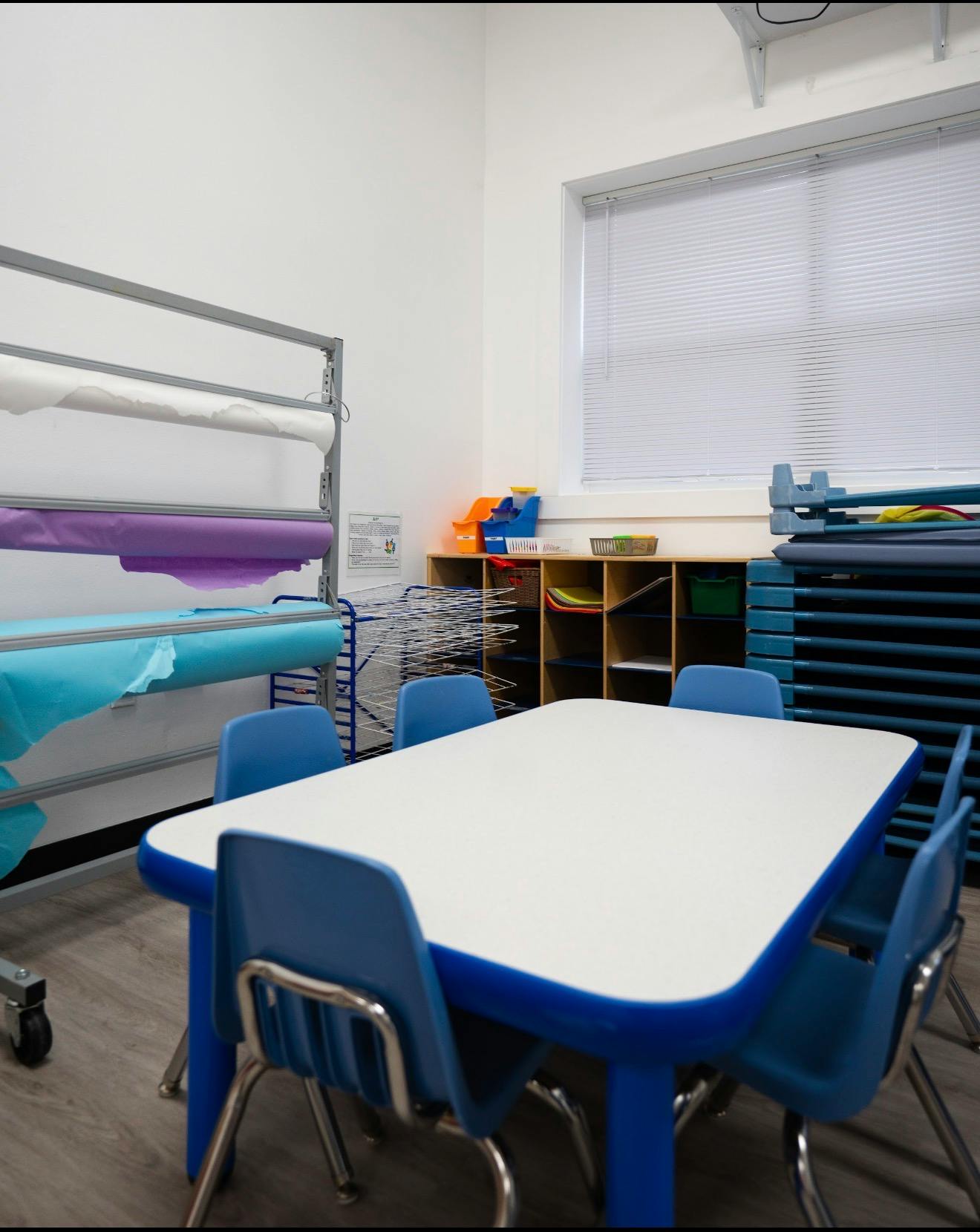 Small table and chairs in a classroom with craft paper rolls and shelving