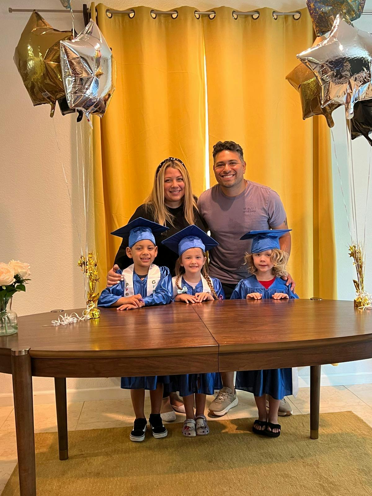 Two adults and three children in graduation caps and gowns posing behind a table