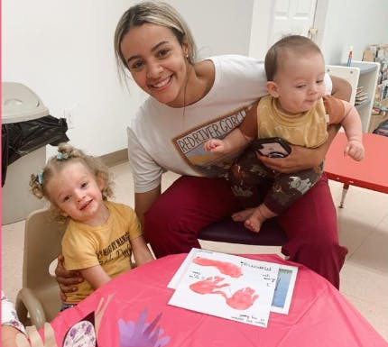 Person holding a child, another child sitting at a table with handprints