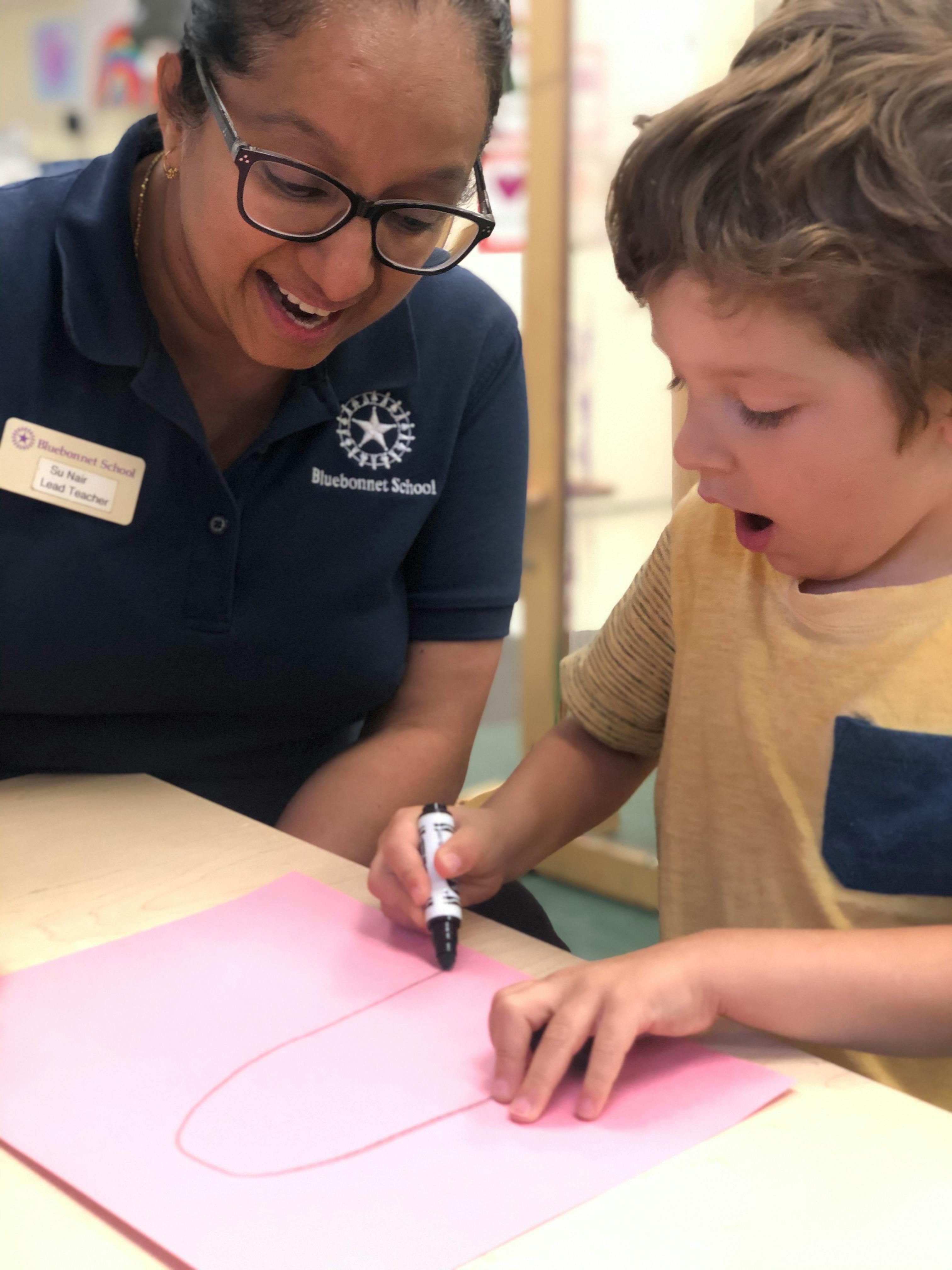 Adult and child drawing on pink paper with a marker