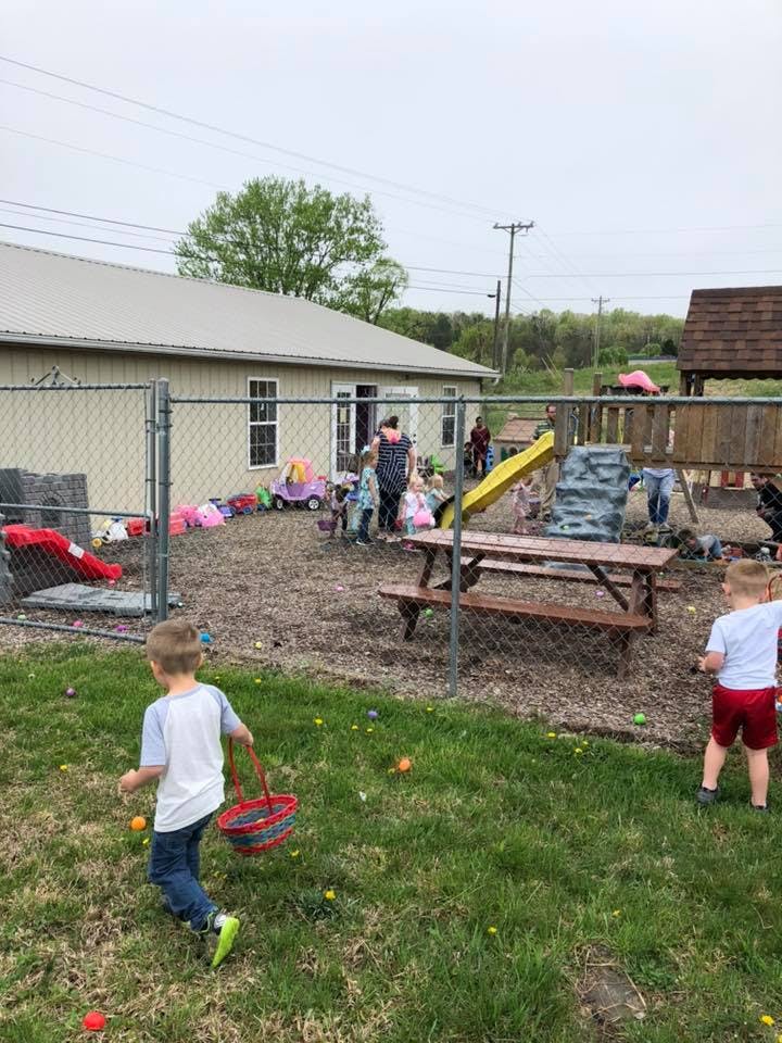 Children and adults in a fenced-in yard with playground equipment