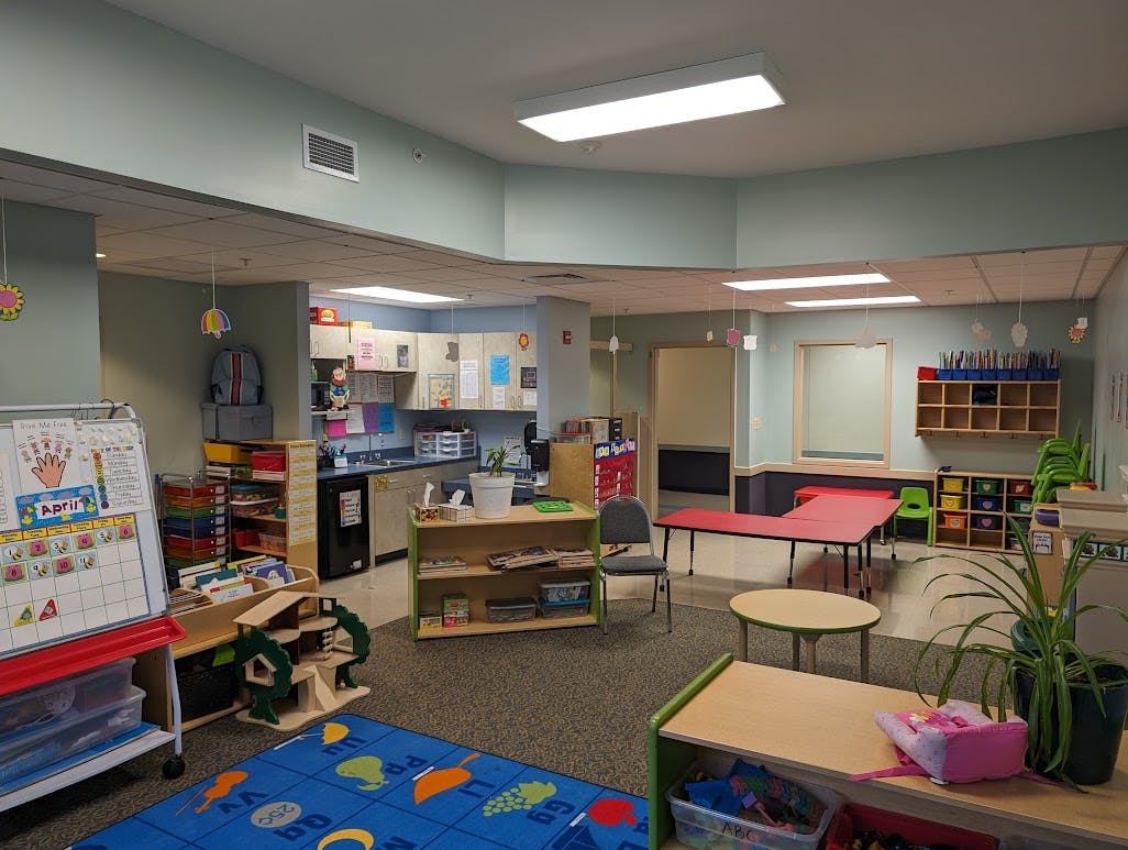 Childcare classroom with play kitchen, tables, and colorful rug