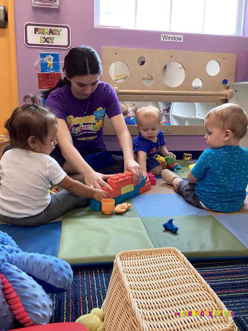 Adult and two children playing with toys on a mat