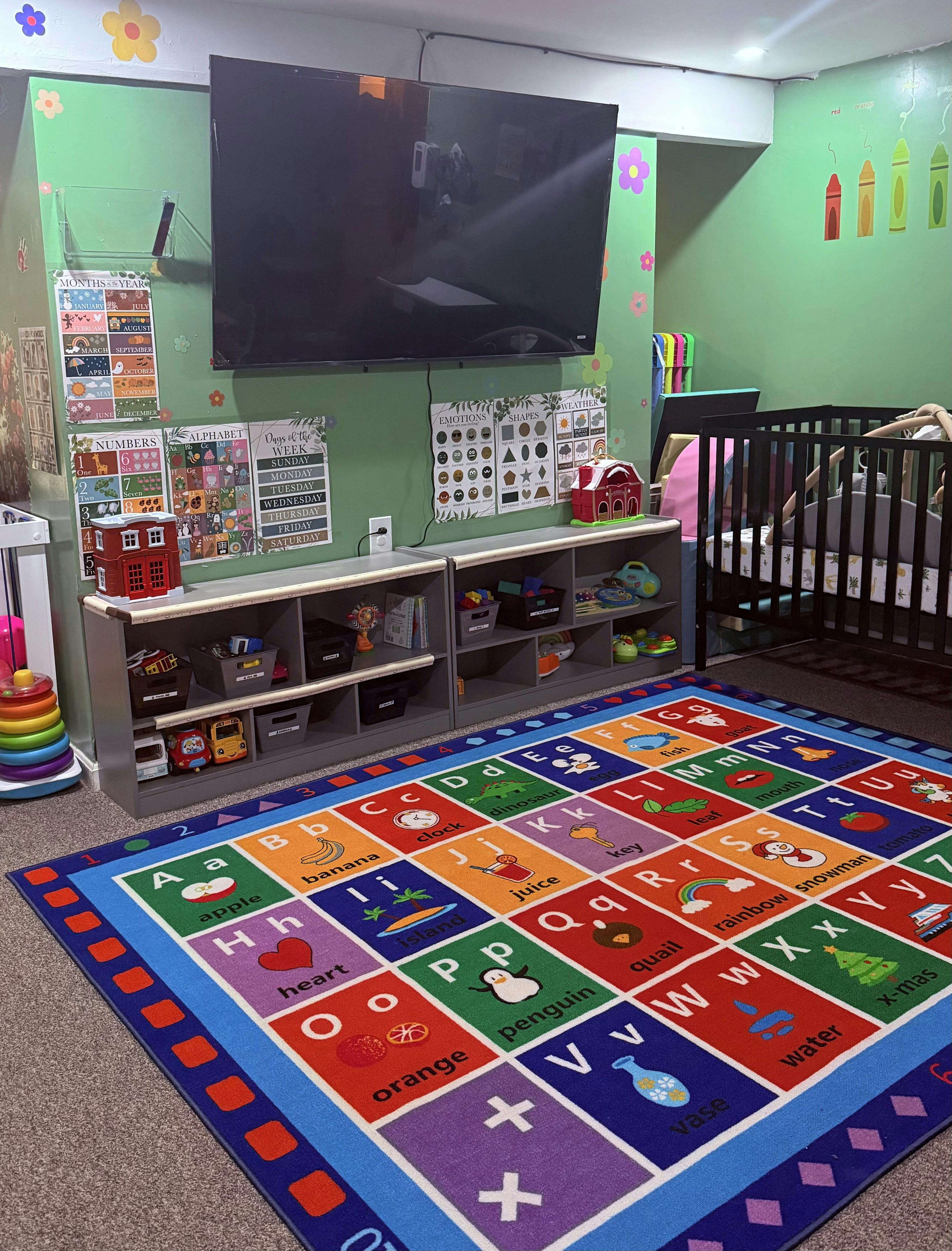 A playroom with an alphabet rug, shelves of toys, charts on the wall, and a crib