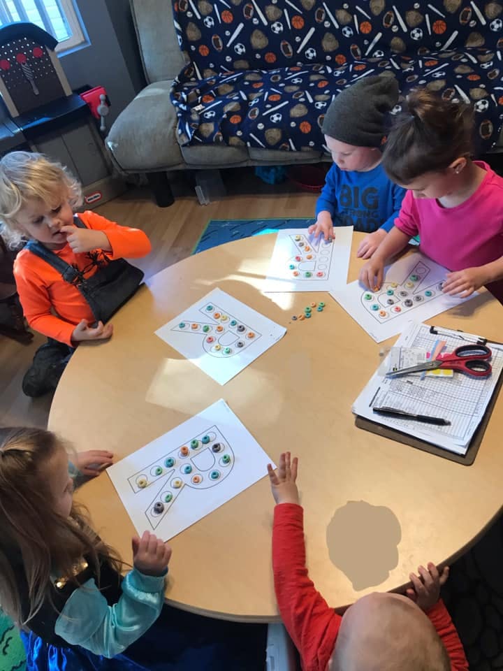 Children sitting around a table doing an activity with letter outlines and beads