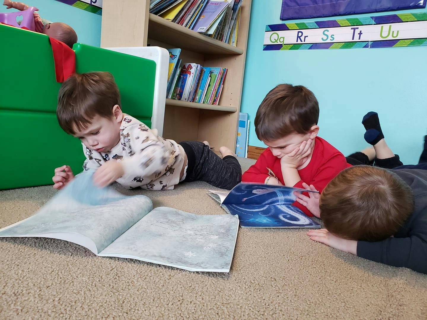 Three children lying on the floor looking at books