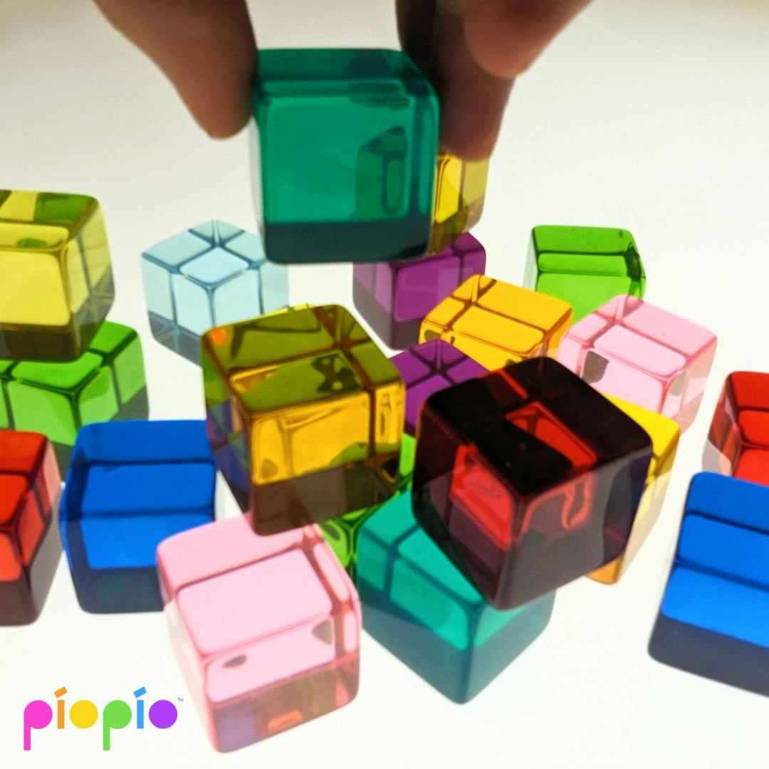 Hand placing a translucent green cube among other colorful cubes