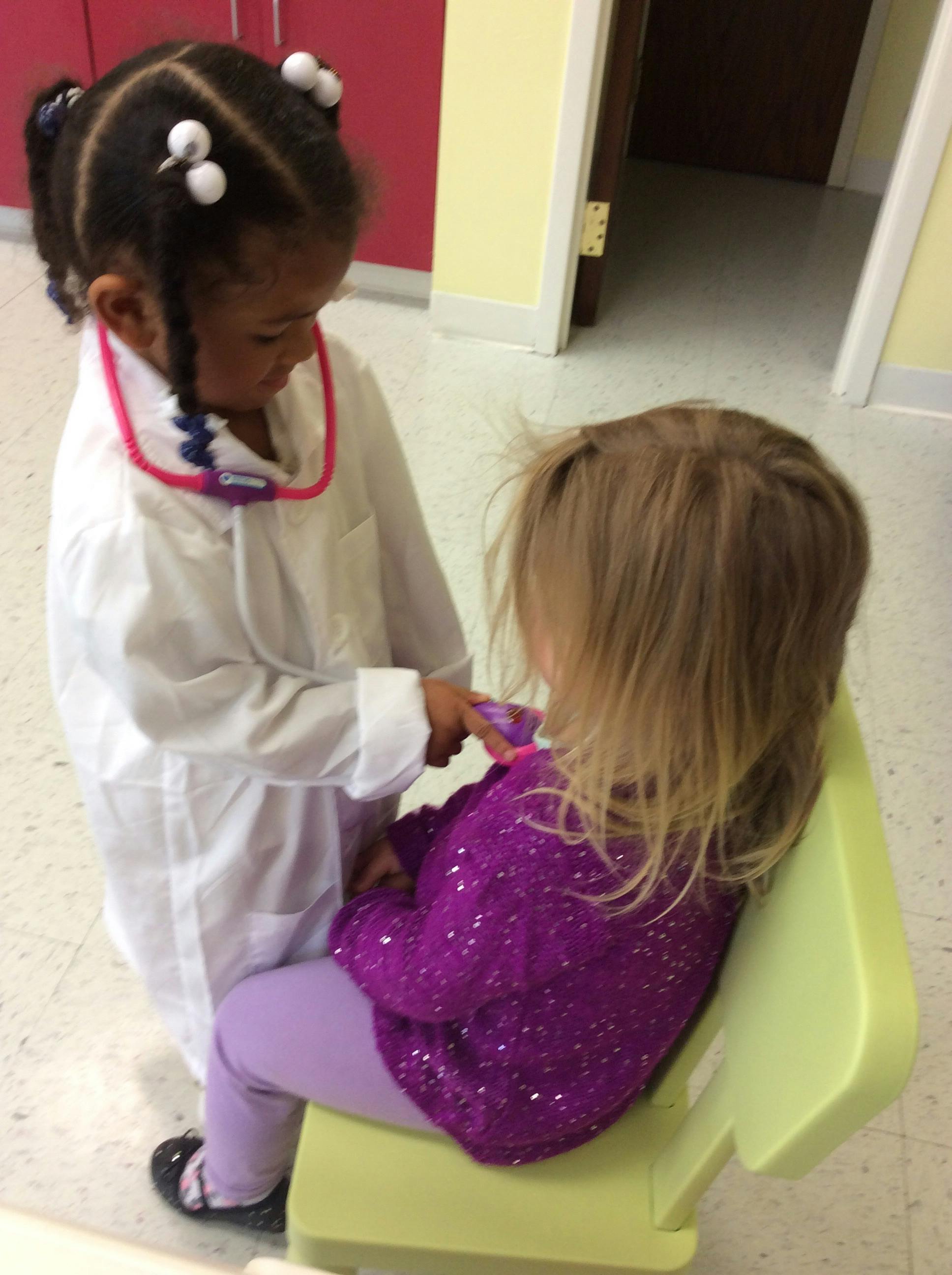 Child in white coat with stethoscope examining another child