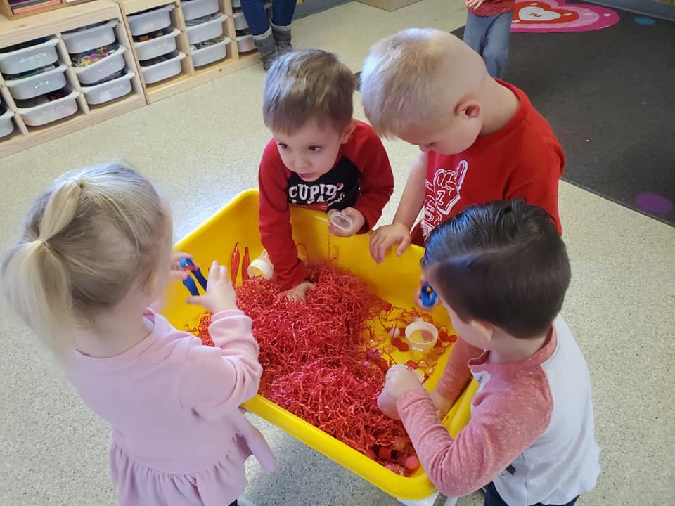 Four children playing with red shredded paper in a yellow bin