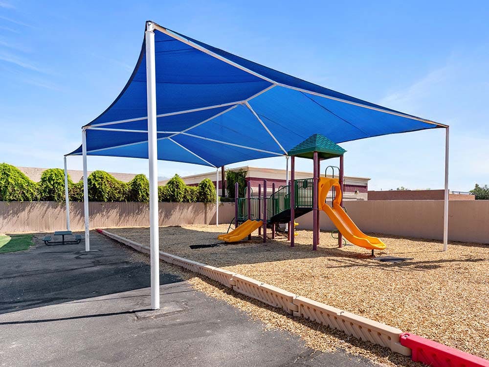 Playground equipment with yellow slides under a blue shade structure