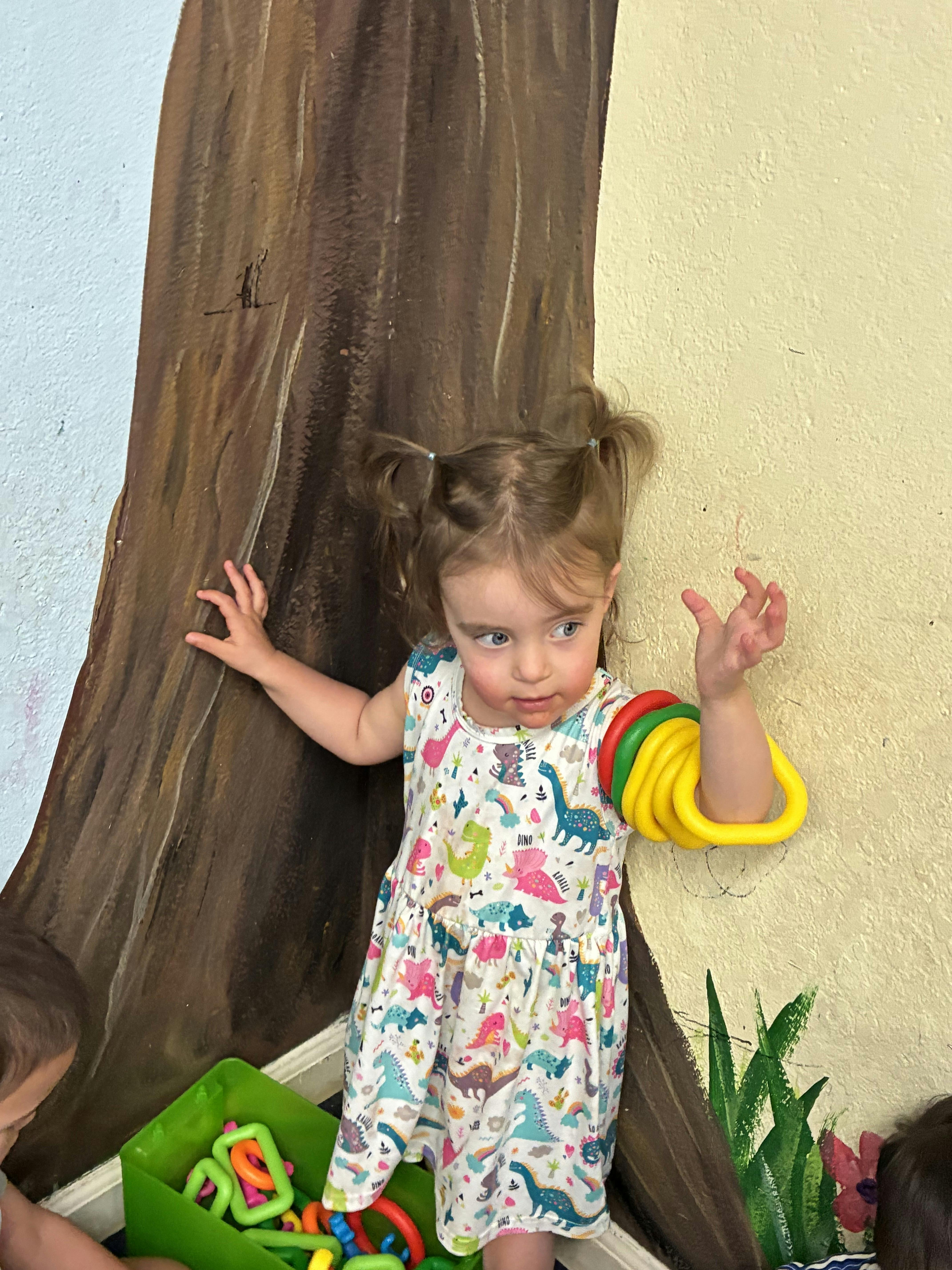 Child in a dinosaur print dress with colorful rings on arm