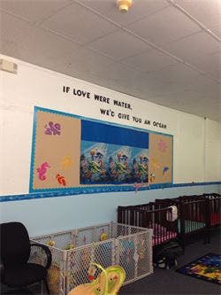 Classroom with cribs and a bulletin board with text "IF LOVE WERE WATER, WE'D GIVE YOU AN OCEAN"