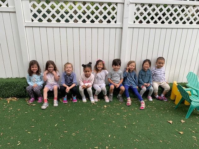 Group of children sitting on grass in front of a white fence