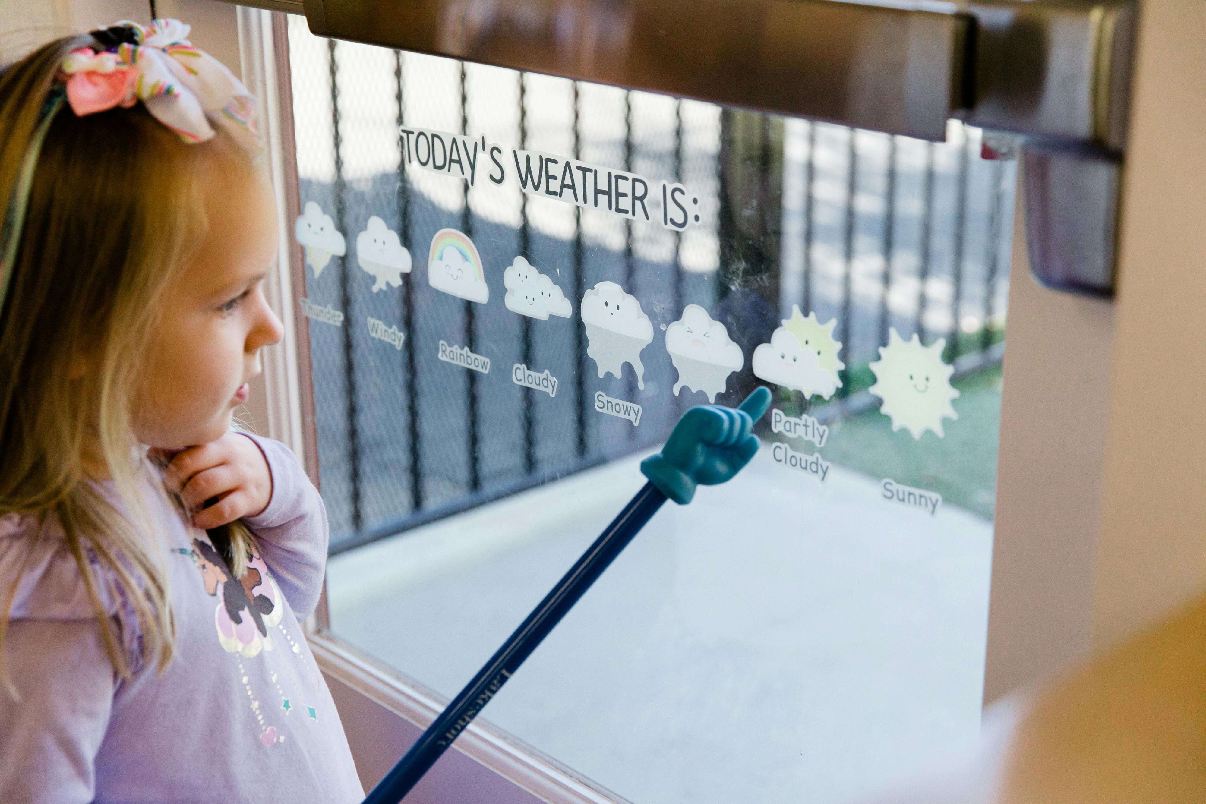 Child pointing to weather icons on a window with a pointer