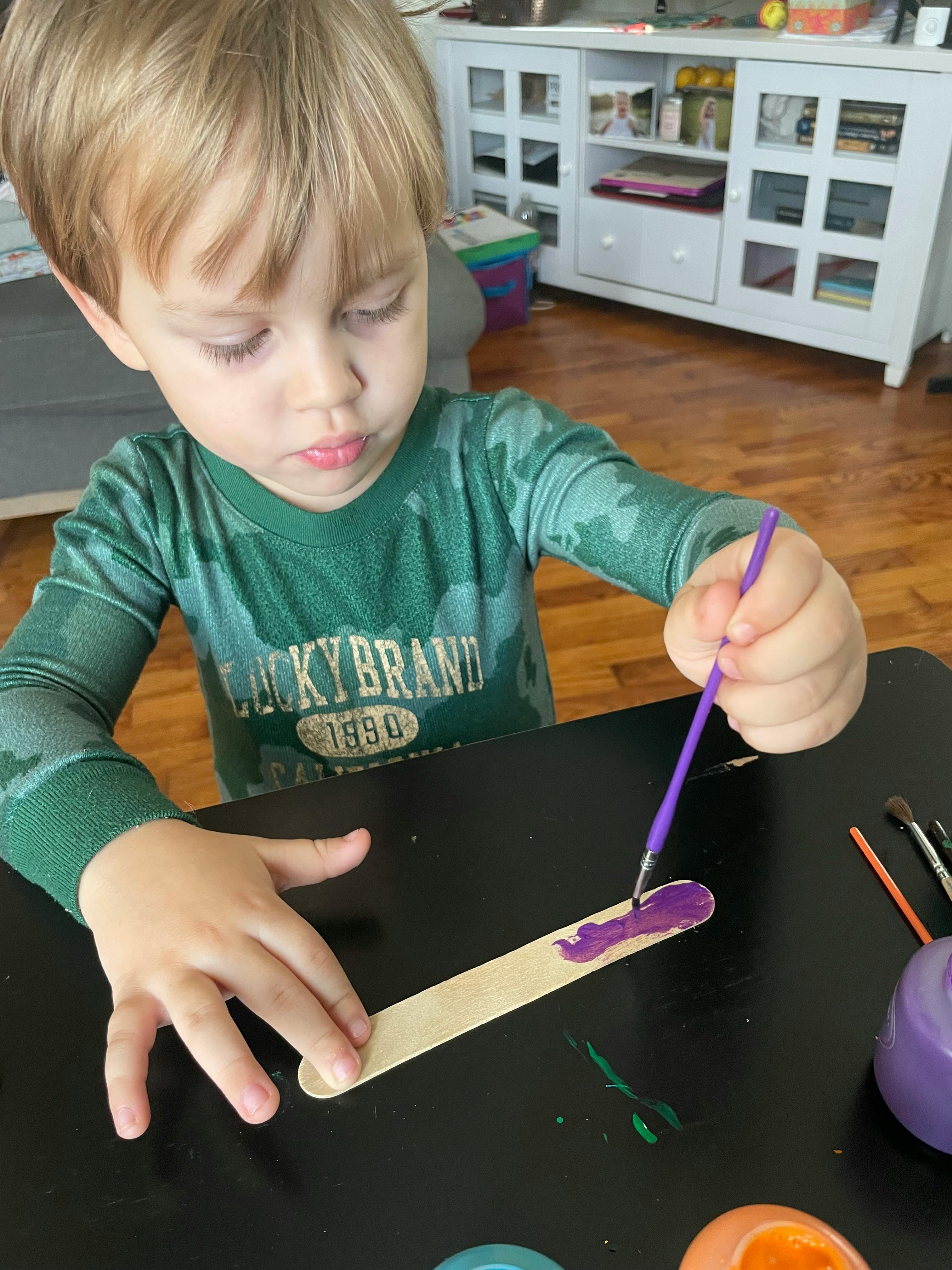 Child painting a craft stick purple with purple paint