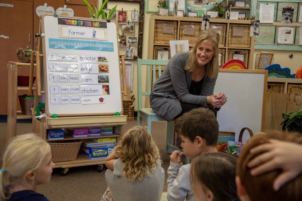 Adult person sitting on a chair in a classroom with children on the floor