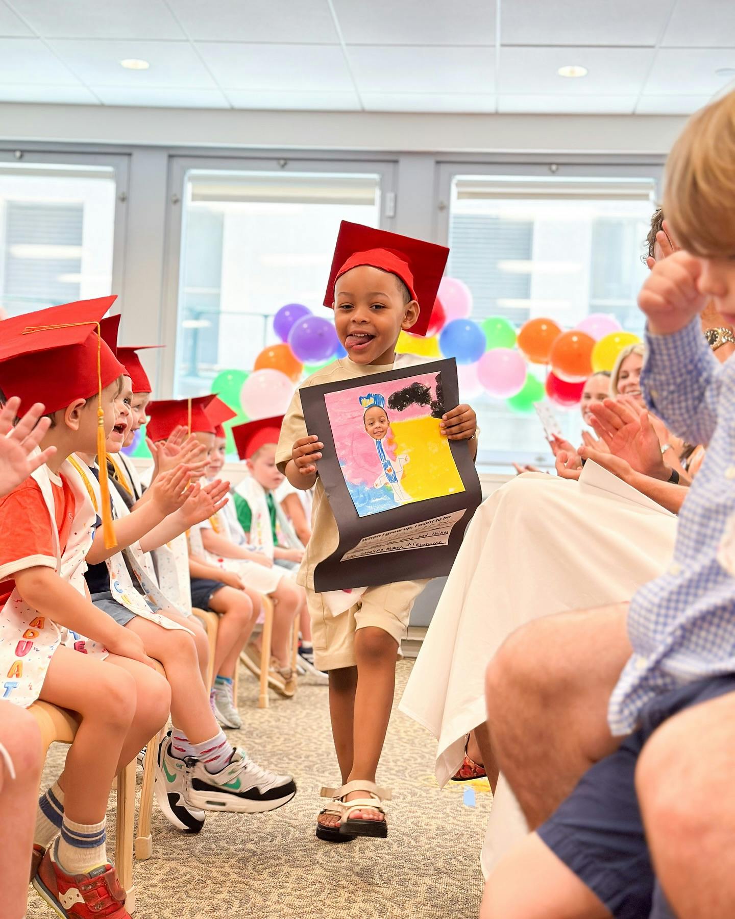 Child in graduation cap holding up artwork while people clap