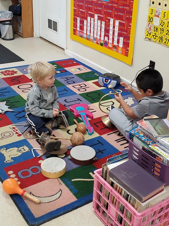 Two children playing with musical instruments on a colorful alphabet rug
