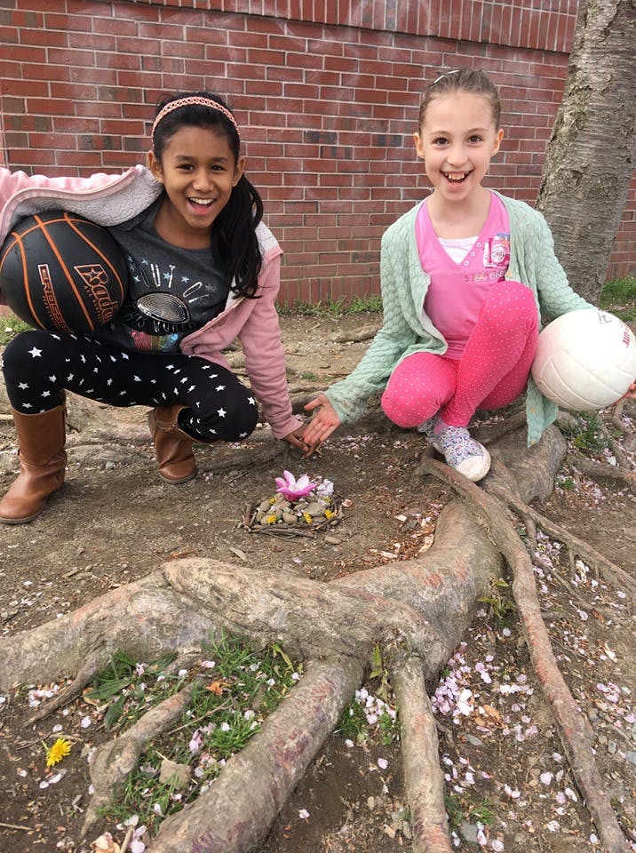 Two children crouching with a basketball and a volleyball, looking at a flower