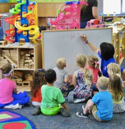 Adult writing on whiteboard for children sitting on floor