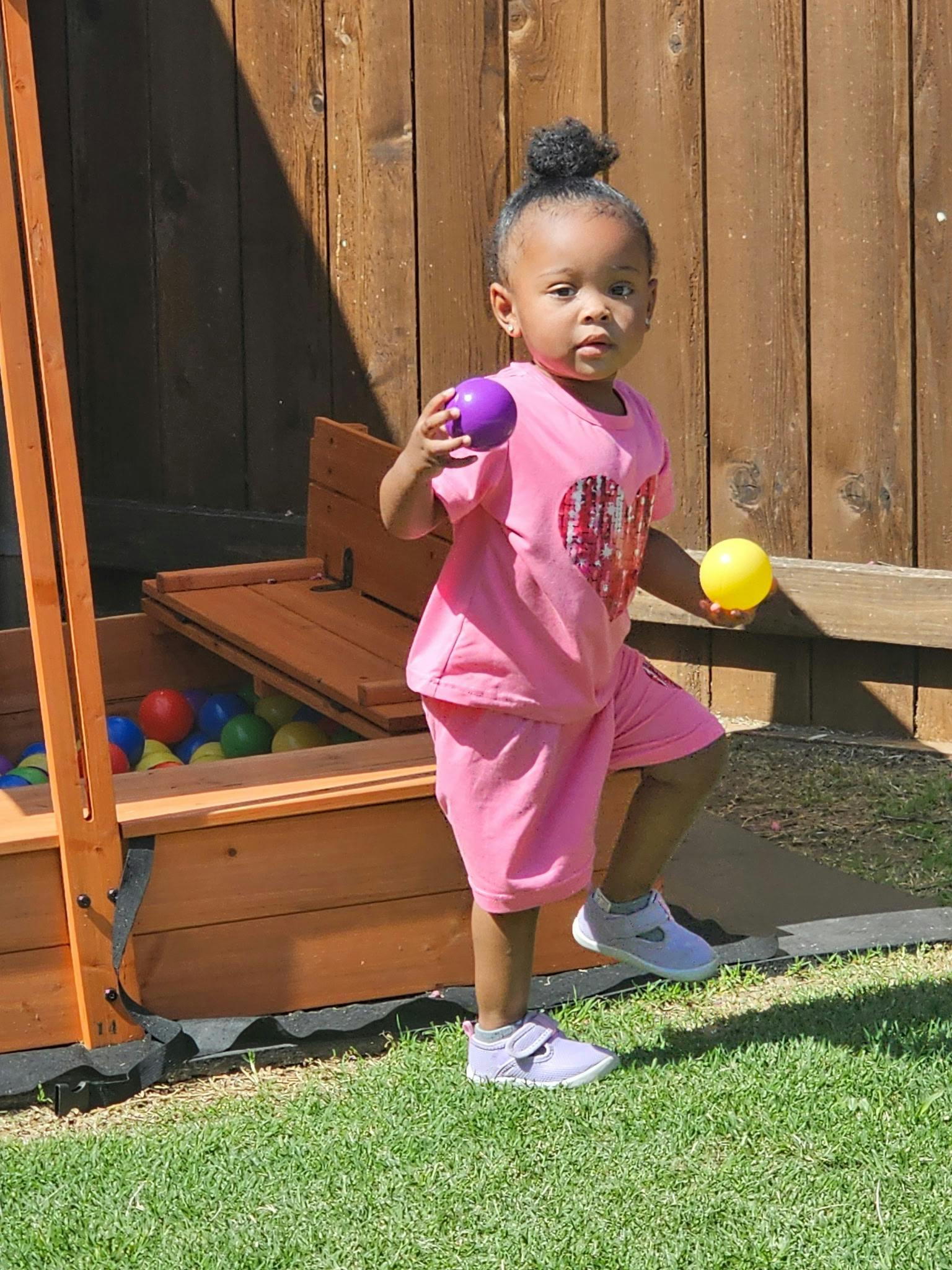 Child playing with colorful balls near a wooden sandbox
