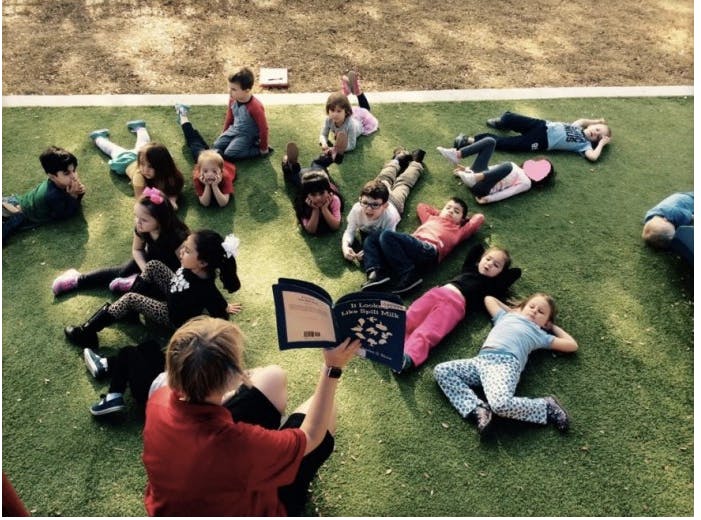 Person reading a book to a group of children on grass