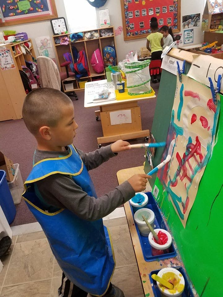 Child in an art smock painting at an easel in a classroom