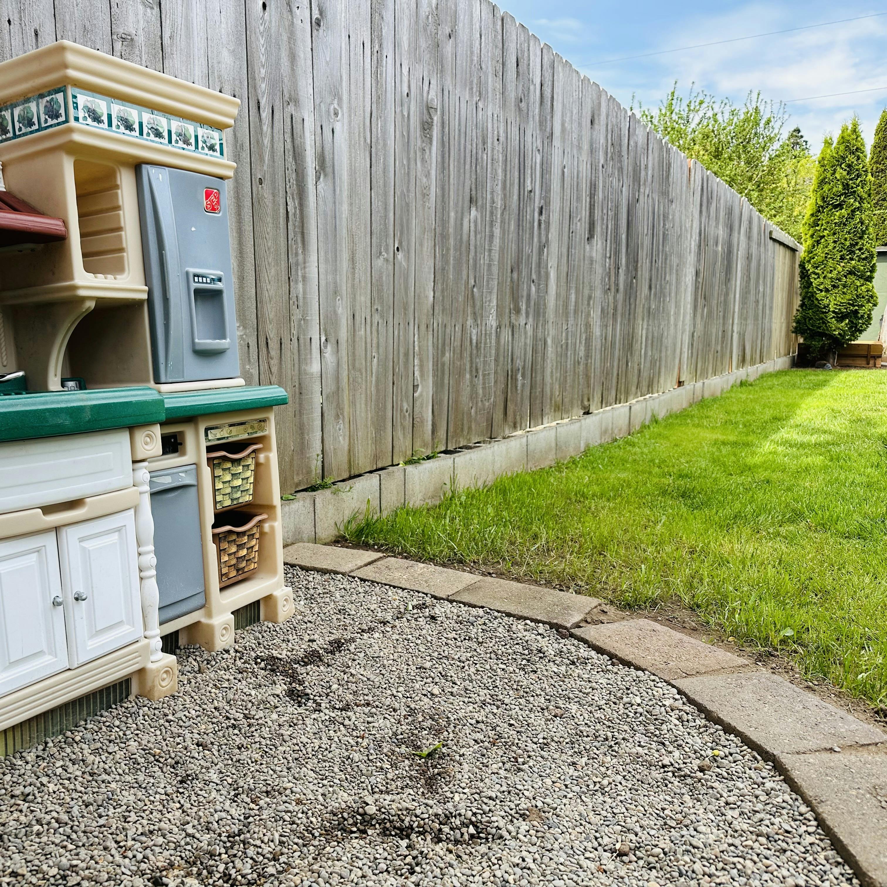 Plastic toy kitchen set in a backyard against a wooden fence