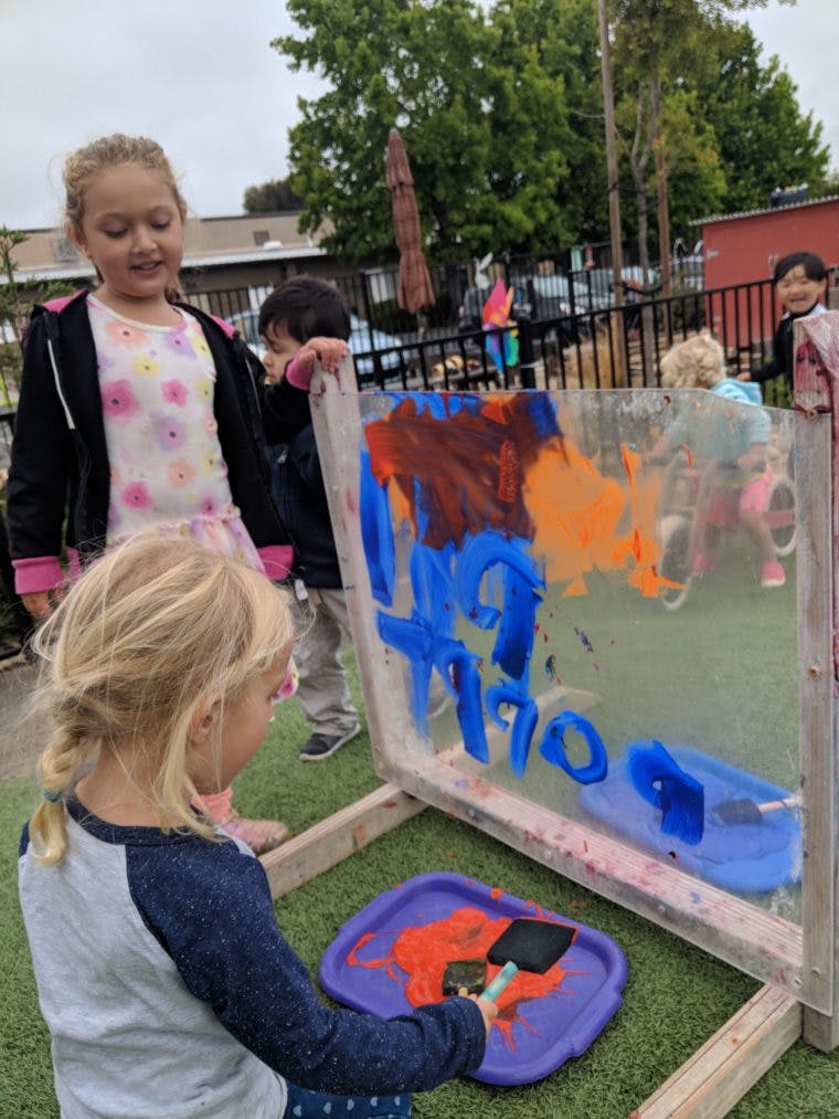 Children painting on a clear easel outdoors