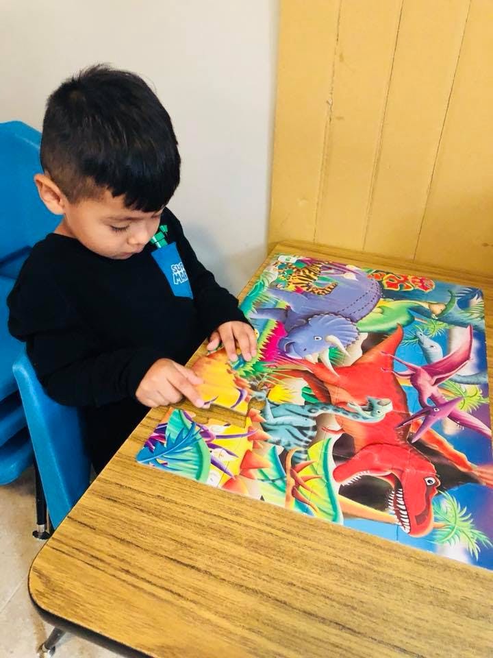 Child playing with a dinosaur puzzle on a table