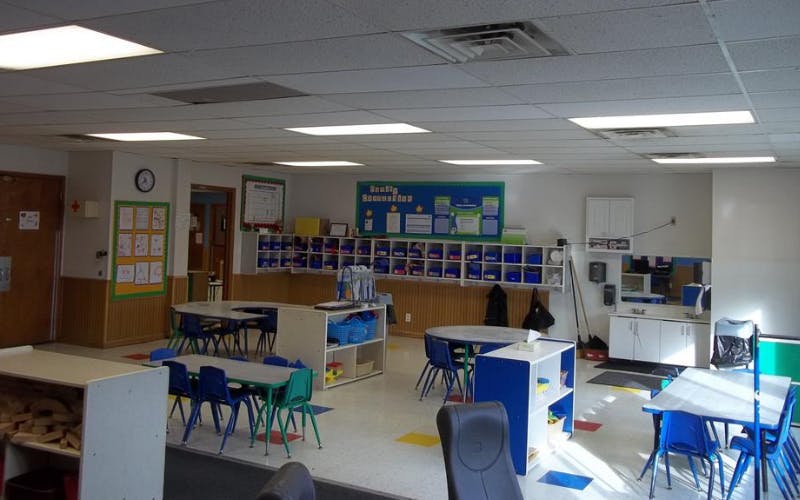 An empty classroom with small tables and chairs for children, cubbies, and bulletin boards