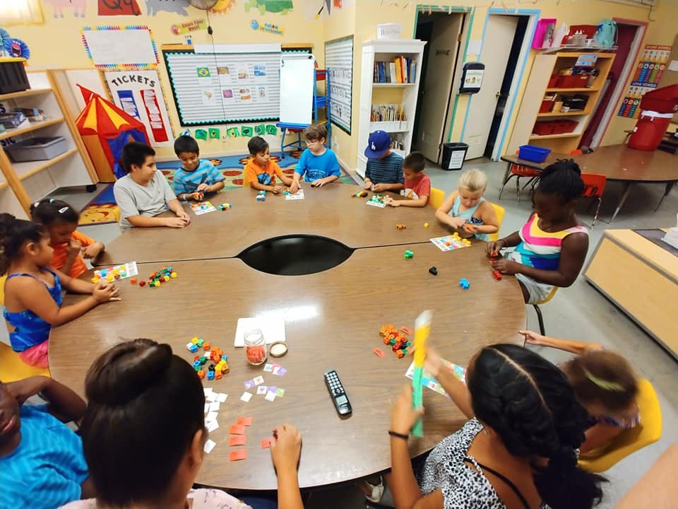 Children sitting around a large table playing with small objects